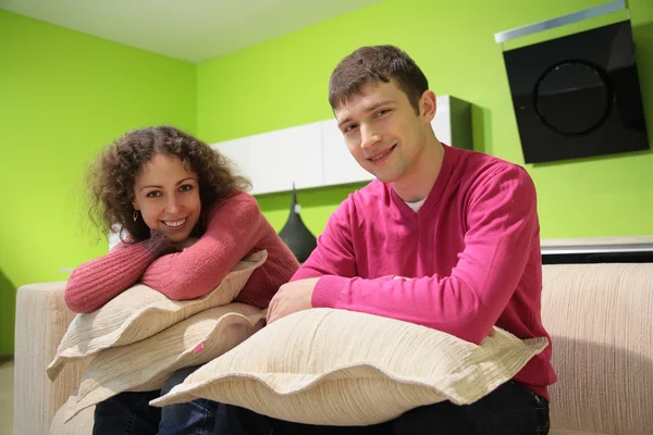 Ζευγάρι, κάθονται στον καναπέ με μαξιλάρια στο πράσινο δωμάτιο — Φωτογραφία Αρχείου