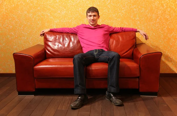 Mladý muž sedí na červené kožené pohovce — Stock fotografie