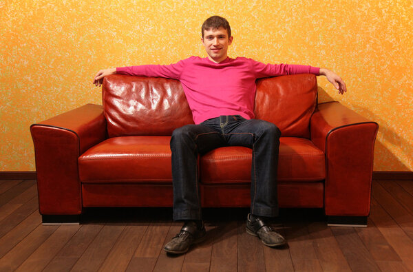 Young man sits on red leather sofa