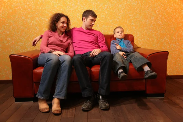 Family seating on red leather sofa — Stock Photo, Image