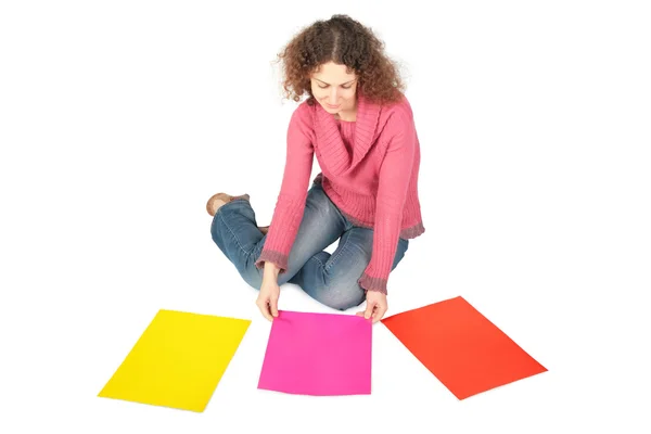 Ung kvinna sitter på golvet med tre flerfärgade pappersark — Stockfoto