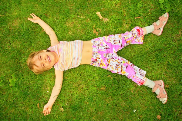 Leende liten flicka ligger på rygg på gräs — Stockfoto