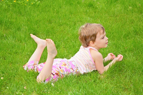 Маленькая девочка лежит на траве на животе — стоковое фото