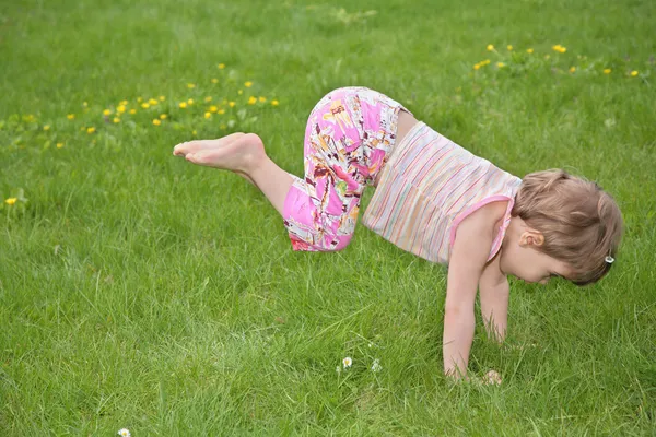 Klein meisje maakt gymnastische oefening op gras — Stockfoto