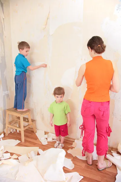 Matka z dziećmi usunąć stare tapety ze ściany — Zdjęcie stockowe