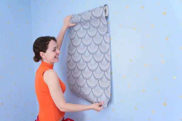 Jonge vrouw probeert muur-papieren aan muur — Stockfoto