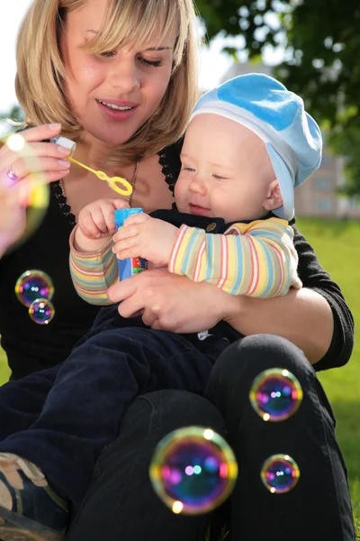 Мать с ребенком на руках запускается с мыльными пузырями — стоковое фото