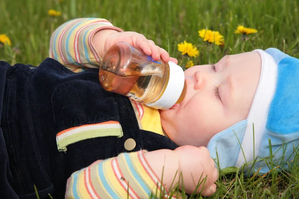 Çocuk çim döşeme bir şişe içki. — Stok fotoğraf