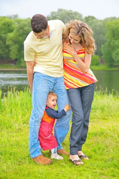 Parents on meadow at water and child between legs — Stock Photo, Image