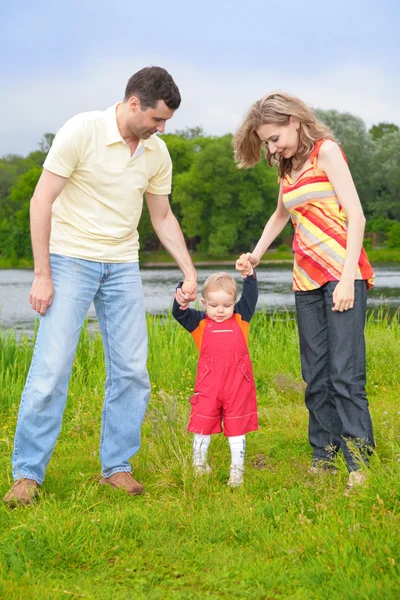 Os pais seguram para mãos de criança que vai na grama — Fotografia de Stock