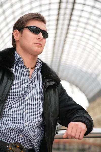 Jovem de casaco preto e óculos de sol — Fotografia de Stock