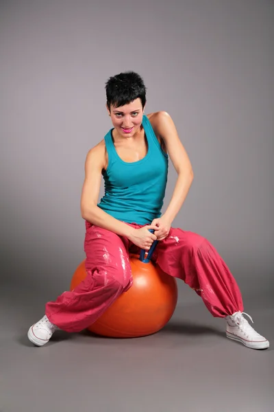Young woman in sportswear sits on orange ball — Stock Photo, Image