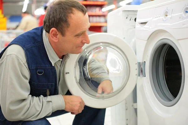 Человек смотрит на стиральную машину в магазине — стоковое фото