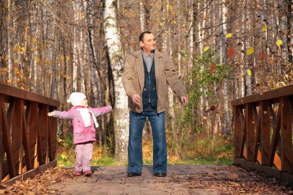 Děda s vnučkou na dřevěný most v lese na podzim — Stock fotografie