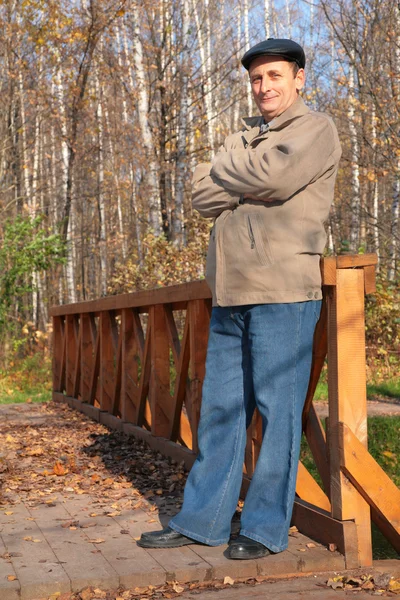 Portrait of elderly man in black hat in wood in autumn on wooden bridge — Stock Photo, Image