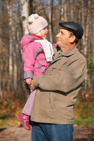 Farfar med barnbarn på händer i trä under hösten — Stockfoto