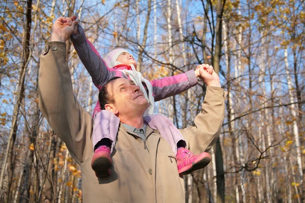 Abuelo con nieta sobre hombros en madera en otoño — Foto de Stock