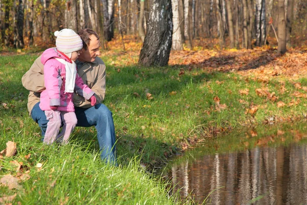 Farfar med barnbarn i trä under hösten ser i vatten — Stockfoto