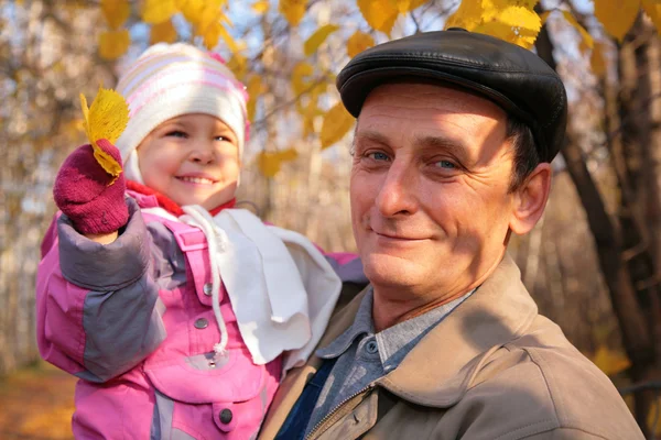 Grandfather with granddaughter on hands with yellow leafs — Stock Photo, Image