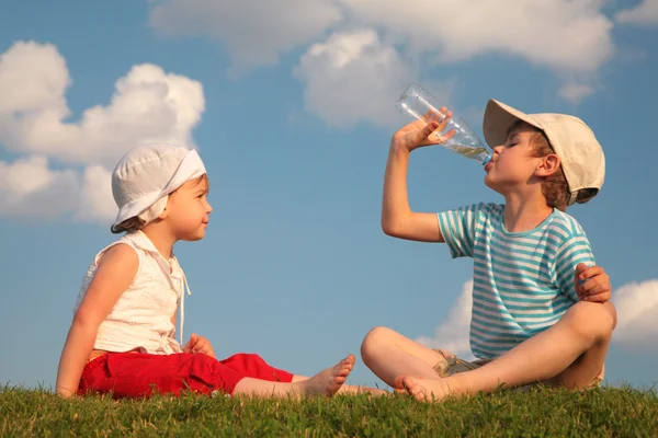 Niño y niña sentarse en la hierba y beber de la botella — Foto de Stock