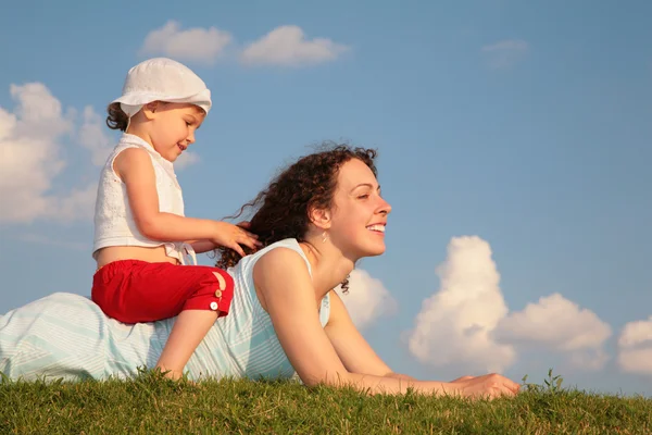 Child sits on back of mother lying on grass — Stock Photo, Image