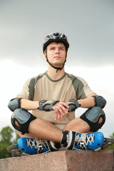 Menino em patins senta-se com pernas cruzadas — Fotografia de Stock