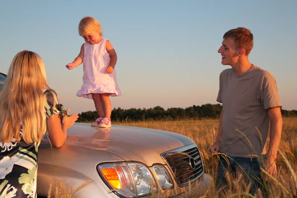 Parents and child on car cowl on wheaten field — Stock Photo, Image