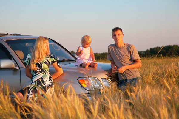 Parents and child sitting on car cowl on wheaten field — Stock Photo, Image
