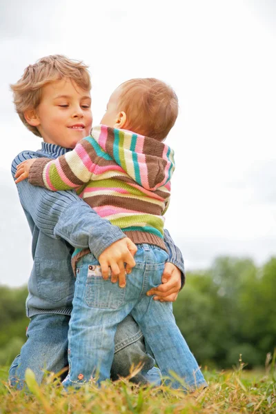 Menino abraça criança na grama — Fotografia de Stock