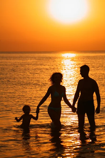Родители с ребенком в море на закате — стоковое фото