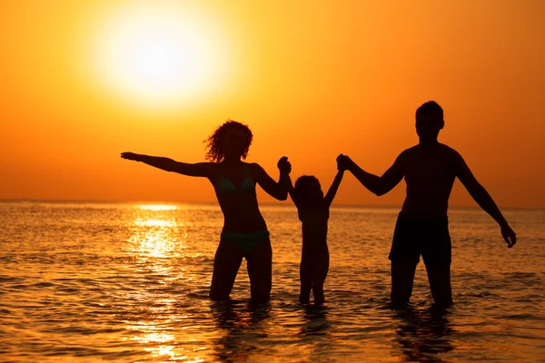 Родители с ребенком в море на закате — стоковое фото