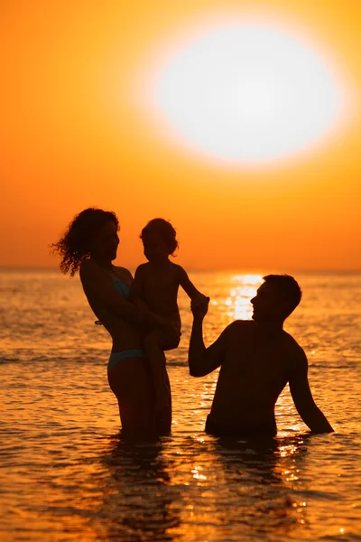 Rodzice z dzieckiem w morze na zachód słońca — Zdjęcie stockowe