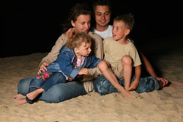 Os pais com crianças sentam-se na areia à noite — Fotografia de Stock