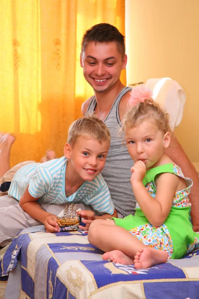 Дети с отцом сидят на кровати в комнате — стоковое фото