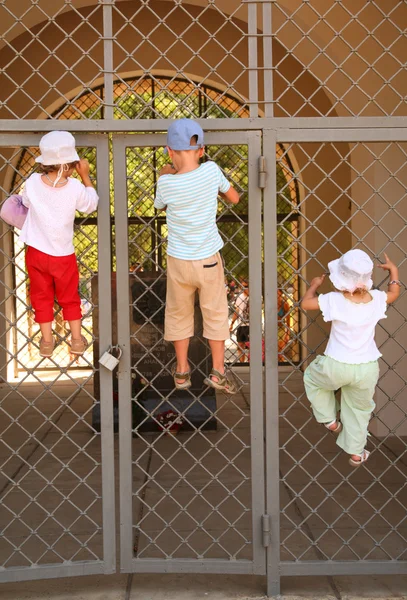 Three children hang on grill of gate — Stock Photo, Image
