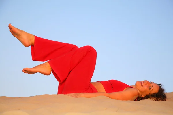 Νεαρή γυναίκα στο κόκκινο βρίσκεται στην άμμο — Φωτογραφία Αρχείου
