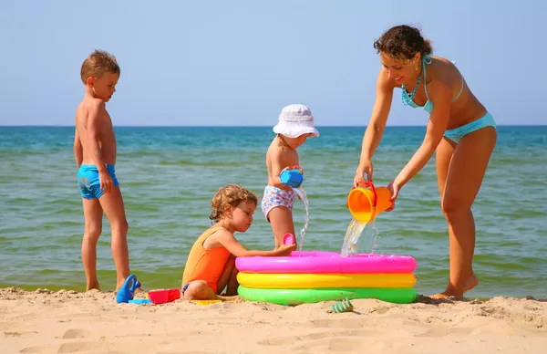 Matka z dziećmi do wlać wodę nadmuchiwany basen na brzegu morza — Zdjęcie stockowe