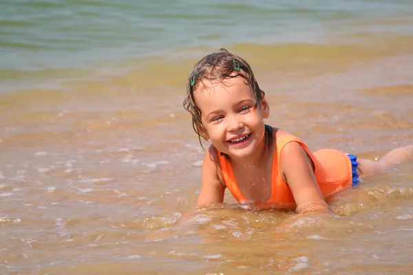 Little girl lies in waves on shore — Stock Photo, Image