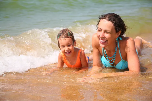 Mother and child lies in wave on shore — Stock Photo, Image