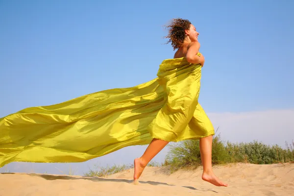 Young girl runs on sand in yellow shawl — Stock Photo, Image