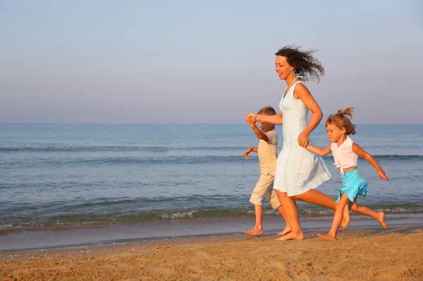 Madre con bambini che corrono sul bordo del mare — Foto Stock