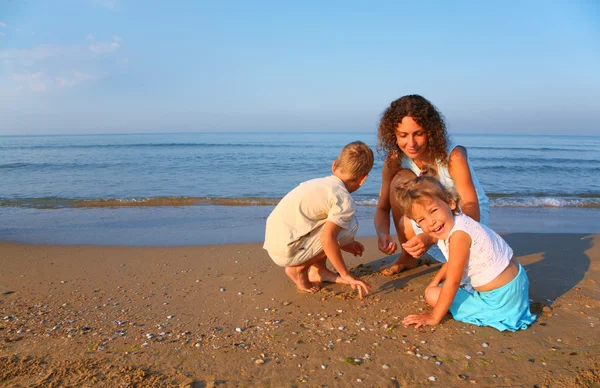La madre gioca con bambini su sabbia a orlo di mare — Foto Stock
