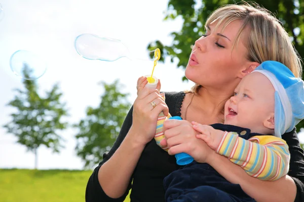 Mãe com uma criança infla bolhas de sabão — Fotografia de Stock