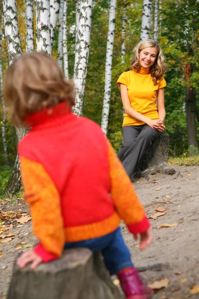 La madre con el niño se sienta en los tallos en la madera en otoño —  Fotos de Stock