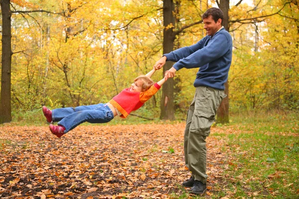 Father rotates child for hands in wood — Stock Photo, Image