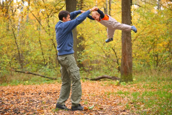 Father rotates child for hands in wood — Stock Photo, Image