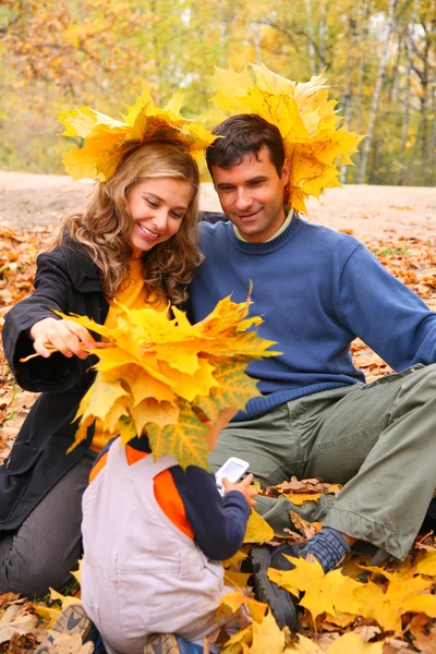 Par e criança com folhas de bordo em madeira de outono — Fotografia de Stock