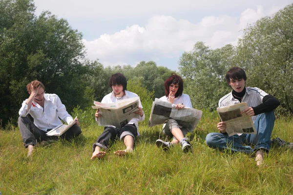 4 人の友人は草の上の新聞を読む — ストック写真