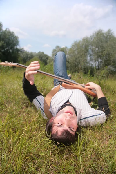 Молодой человек лежит с гитарой на траве — стоковое фото