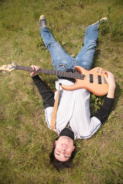 Mladý muž stojí s kytarou na trávě — Stock fotografie